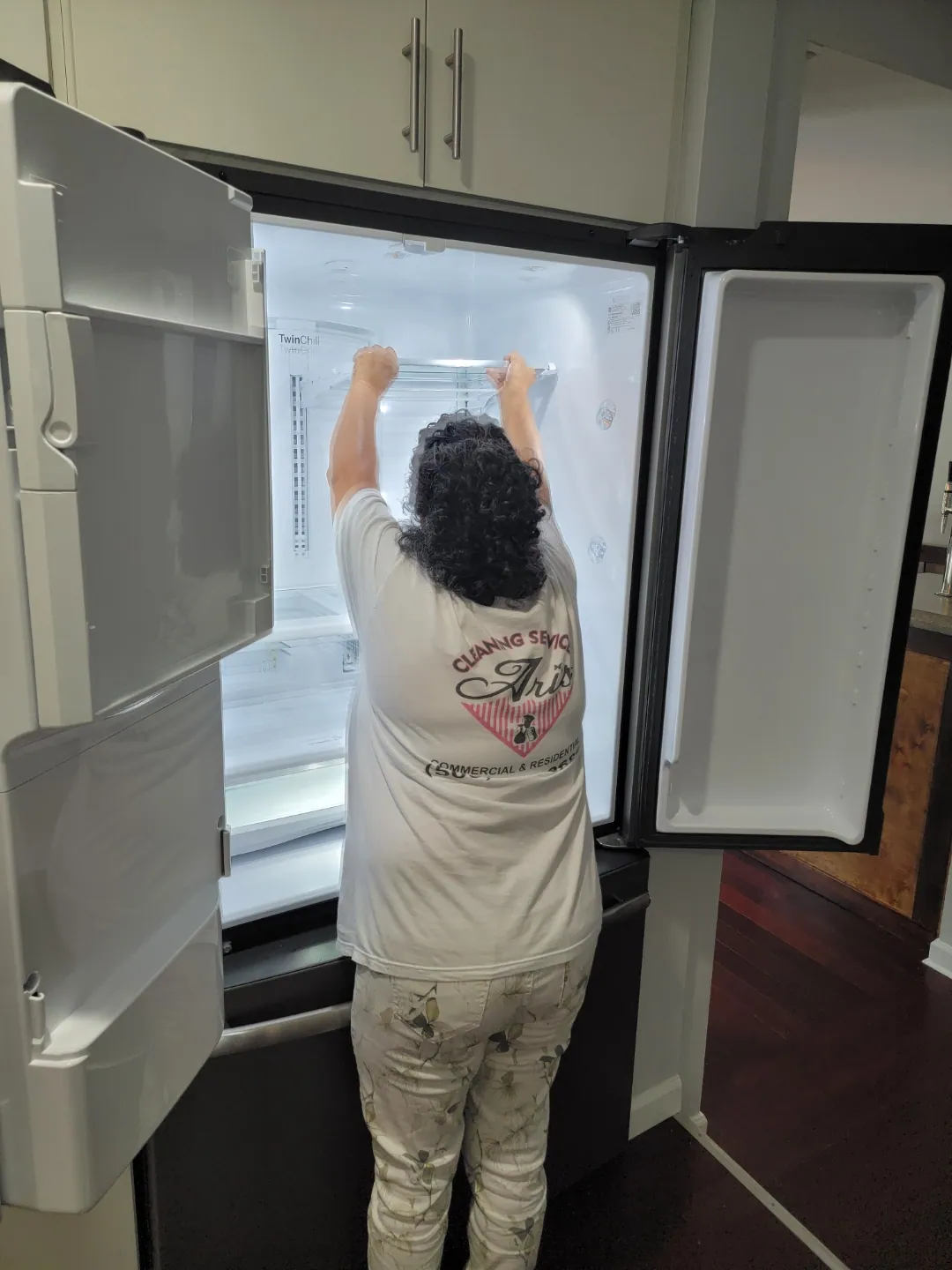An Ari's Cleaning team member in a branded shirt detailing the inside of a refrigerator